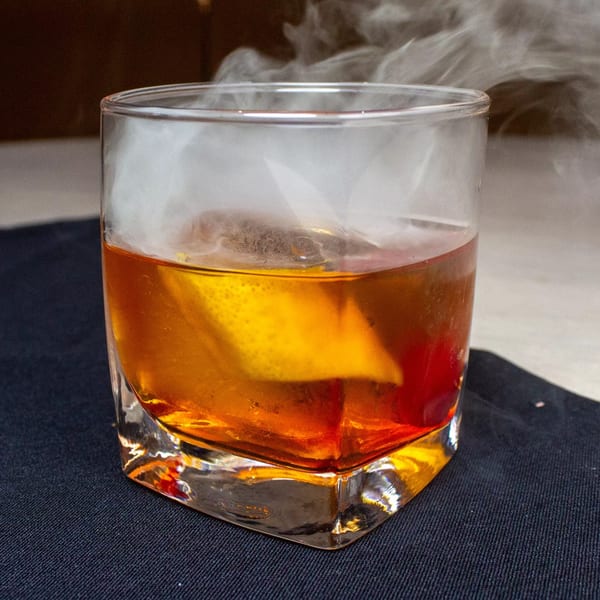 Smoked old fashioned cocktail with an orange peel, served in a rocks glass on a dark napkin.