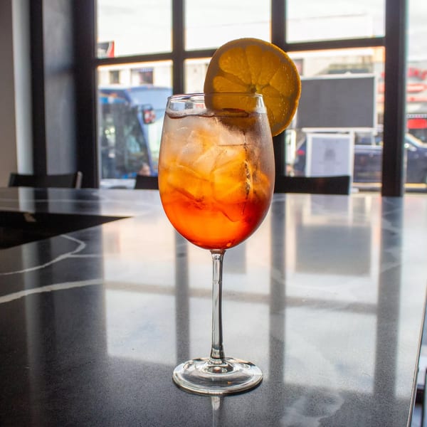 A vibrant orange cocktail with ice and an orange slice, on a dark marble table by a window.