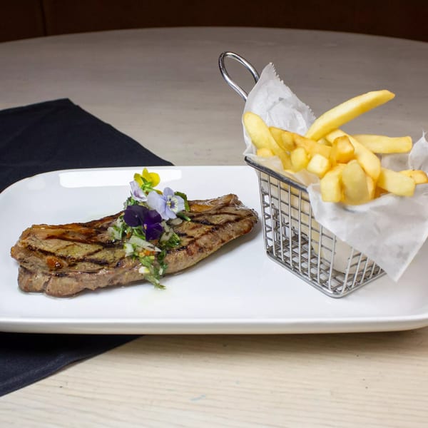 Grilled steak with edible flowers and a side of french fries in a metal basket.