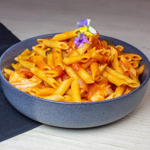 Penne pasta with shrimp in a red sauce, garnished with edible purple and yellow flowers.