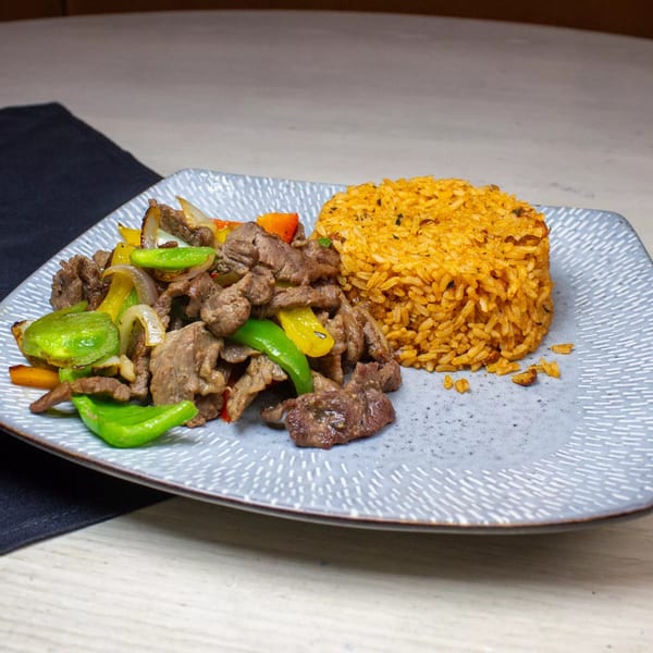 Stir-fried beef with green and yellow bell peppers, onions, and a side of seasoned rice.