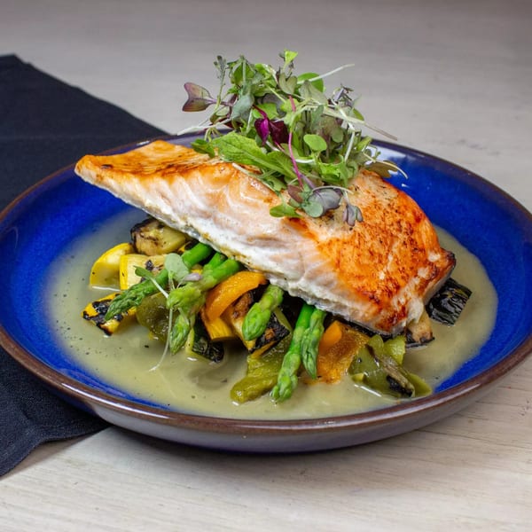 Pan-seared salmon with grilled asparagus, squash, and peppers in a light sauce on a blue plate.