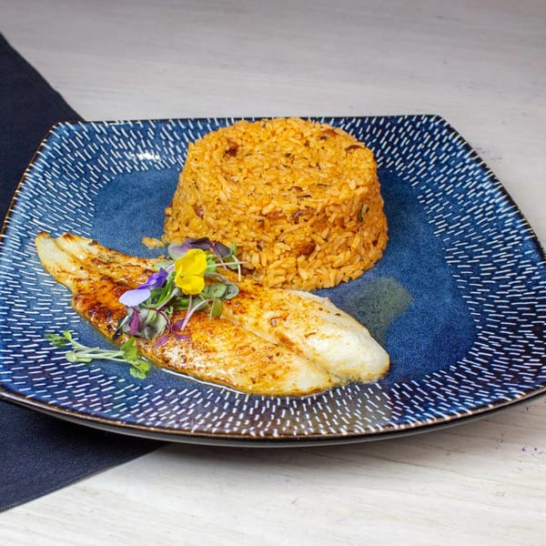 Grilled fish fillet with seasoned rice, garnished with edible flowers and microgreens on a blue plate.